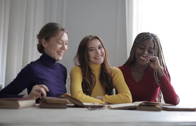 Three diverse students are gathered around a table, smiling and discussing scholarship opportunities on a laptop screen, with an open textbook and notebooks nearby.