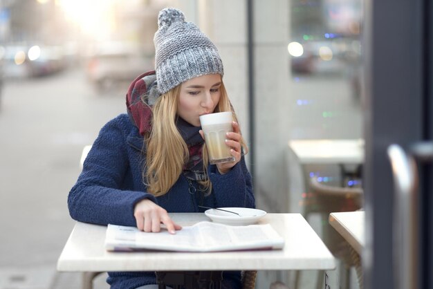 A college student sitting at a cafe table in a bustling European city, studying a textbook while sipping coffee, representing the daily life and academic pursuits of a student abroad.