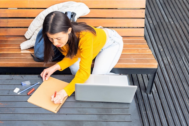 A college student sitting at a desk covered with textbooks and a laptop, looking thoughtfully at a course catalog and planning their semester schedule with a calendar and highlighter nearby.