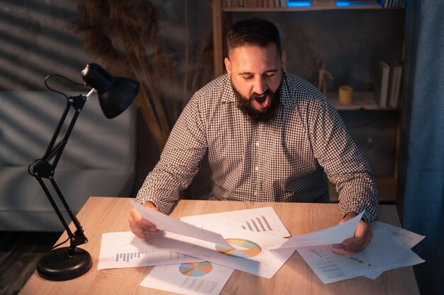 An individual is seated at a desk, thoughtfully reviewing financial documents with graphs and charts. They are using a calculator and have a pen in hand, indicating focused analysis and planning. The scene conveys a sense of diligence and careful consideration of investment options.