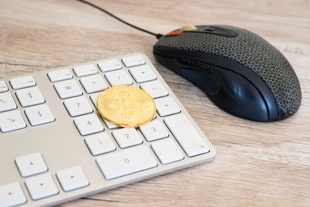 A close-up shot of a physical Bitcoin token resting on a computer keyboard, with a screen displaying cryptocurrency market charts in the background. The lighting is bright and focused on the token, highlighting its golden color and intricate design.