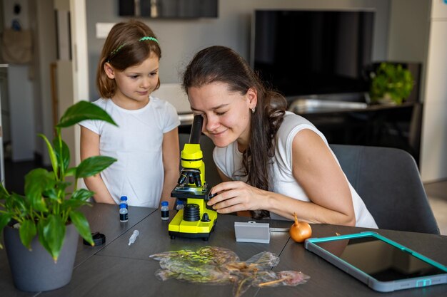 A parent and child sitting at a table, working together on a science project. The child is holding a beaker, and the parent is pointing at a diagram. The scene captures a supportive and collaborative learning environment at home.