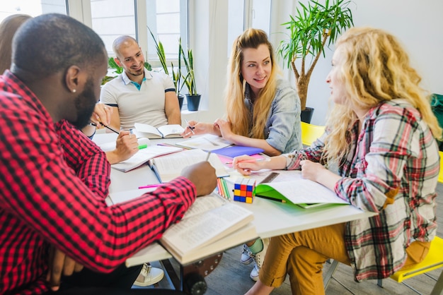 A group of teachers and education experts are gathered around a table, reviewing documents and charts related to curriculum standards. The scene is well-lit, and the atmosphere is collaborative and focused.