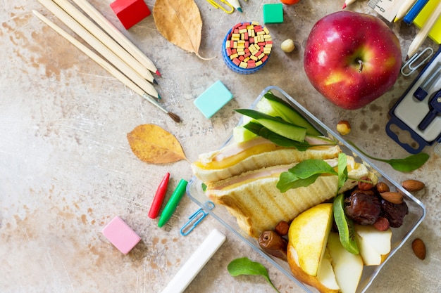 Close-up shot of a school lunch tray featuring a variety of colorful fruits and vegetables, a whole-grain sandwich, and a carton of milk. The focus is on the presentation and nutritional value of the meal.