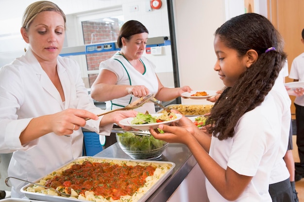 A school cook preparing a large batch of freshly cut vegetables in a school kitchen. The focus is on the preparation process of healthy school meals.