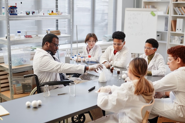 A professor is working with two college students in a university laboratory, surrounded by scientific equipment and computers. The students are dressed casually and appear to be analyzing data and discussing their findings. The atmosphere is collaborative and focused on scientific discovery.