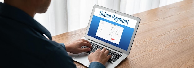 A person using a laptop to set up online banking transfers, focusing on the recurring transfer setup screen. The background shows a comfortable home office environment with financial books and a calculator.