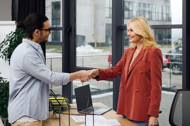 A friendly bank representative is seen shaking hands with a customer across a desk, with a computer showing loan terms in the background. The lighting is bright and professional, illustrating a successful negotiation.