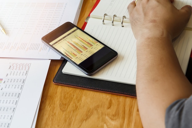 A person using a budgeting app on their smartphone, with charts and graphs displaying income, expenses, and savings. The setting is a coffee shop, emphasizing the convenience of mobile budgeting while on the go.
