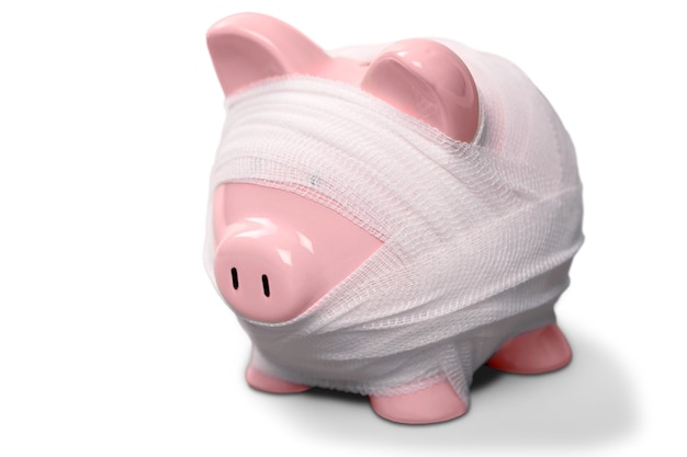 A piggy bank with bandages and a first aid kit next to it, symbolizing the concept of an emergency fund for unexpected expenses.