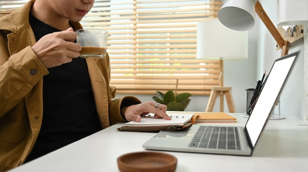 A person writing down financial goals in a notebook on a desk with a laptop and a cup of coffee. The person is focused and determined. The notebook has headings like 