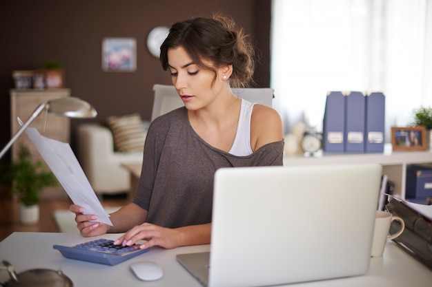 A person sitting at a desk with a laptop, reviewing a spreadsheet with debt information and budget figures. The scene suggests careful planning and organized effort in managing finances and implementing a debt payoff strategy.